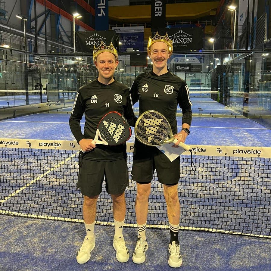 Twee spelers in hetzelfde tenue met kroontjes en hun rackets, bij het net op een baan van Playside